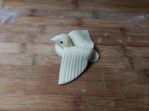 再捏出小鸟嘴，两边各按下一粒黑豆做小鸟眼睛