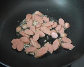 然后加入大蒜爆香，爆香后加入鸡肉肠，翻炒一下。
