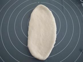 取其中一个面团，用手轻轻按压排气，再用擀面杖擀开，使其成为一个椭圆形。