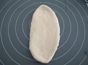 取其中一个面团，用手轻轻按压排气，再用擀面杖擀开，使其成为一个椭圆形。