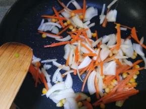 锅中留底油，下洋葱爆香，再加入胡萝卜丝和玉米粒炒软。