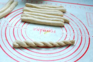 把每一个小剂子都揉成长条，盖上保鲜膜，静置10分钟。静置好的面团会非常容易搓长，不易断裂。醒发好了，开始搓成麻花吧。反方向，左手向下用力搓，右手向上用力搓，然后捏住两头提起来，很自然的就会扭在一起。