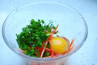 胡萝卜借助工具擦成丝，或者如果你刀工不错的话也可以切成细丝。小香葱切成葱花，放在一个大一点儿碗内，打入一颗鸡蛋。