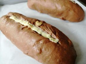 面包胚发酵有差不多两倍大，用面包割刀在面包表面割一条口子，把软化的黄油挤入。室温高，直接把黄油放入裱花袋中，用手掌捂住一会儿，黄油就能软化了