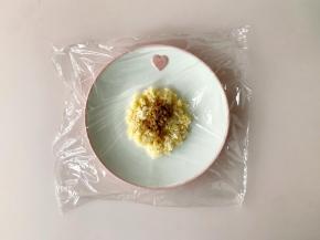 待杂粮饭稍微放凉后，撕一片保鲜膜，中间放入50克的杂粮饭，铺平，中间放上一小勺儿童肉松。