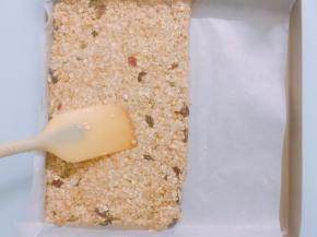 烤盘中铺上油纸，倒入混合好的水果麦片，用硅胶刮刀轻轻压平
