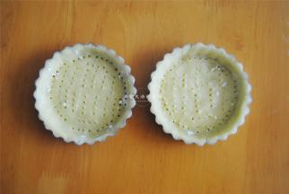 将挞皮放入盘里，往下轻压使其贴紧模具，去掉多余的挞皮，用叉子扎出气孔，防止烤的时候鼓起。