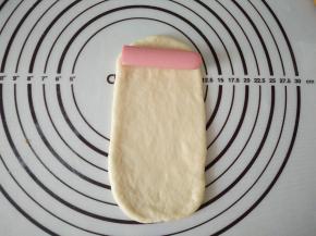 取一个松弛好的面团擀成椭圆形，放入一段香肠 。