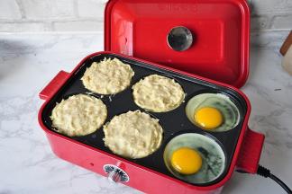 多功能料理盒提前预热一下，刷点油，然后将拌好的土豆放入盘中，我这个盘模有六个，我只放了四个，剩下的两个煎了鸡蛋。您如果不煎蛋的话，可以放入点水，也防止锅干烧，如果没有这种锅，可以用平底锅代替。