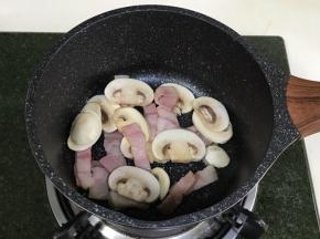 开火，锅中倒入橄榄油，放入培根和口蘑翻炒至微微变色。