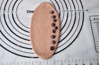 松弛后的面团，用擀杖擀成椭圆形，翻面后，放入巧克力豆，注意是放一侧