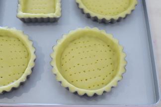 取一小片，放入8厘米的塔模内，用手按压好塔皮形状，利用刮刀刮取多余的塔皮，用小叉子叉一排排小孔。