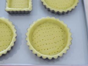 取一小片，放入8厘米的塔模内，用手按压好塔皮形状，利用刮刀刮取多余的塔皮，用小叉子叉一排排小孔。