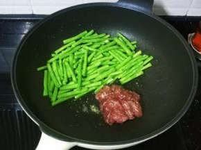 将豆角推锅边，放入牛肉片