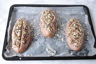 将面包表面喷水，撒黑白两色芝麻和麦片装饰。用刀片随意划上自已喜欢的花纹。