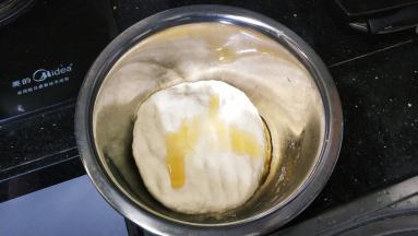 20分钟后拿开湿布，倒入2勺子油，将面团揉至光滑