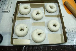 然后将面团另一端放置在擀开的尾部，用擀开的那一边将另一边包裹起来，捏紧，形成圆环形。摆放在垫有油纸的烤盘上。油纸可以提前裁好，可以提着油纸拿起贝果。