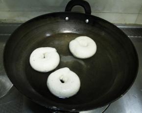 然后把发酵好的贝果，拎起油纸，倒扣在锅里，一锅煮三个，动作要快，不要怕，不会溅出来，然后把油纸拿掉，放回烤盘，煮30秒，然后用漏勺翻面，继续煮30秒。