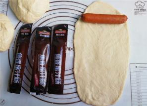 把面团揉圆，用擀面杖把面团擀成跟香肠一样长宽度，再把香肠卷起来。