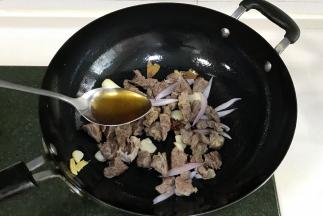 接着放入1段大葱和洋葱翻炒片刻，倒入牛腩和1勺料酒翻炒约20秒。
