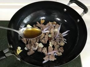 接着放入1段大葱和洋葱翻炒片刻，倒入牛腩和1勺料酒翻炒约20秒。