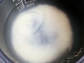 用电饭锅自带的量杯，量半杯大米，清洗干净，倒入电饭锅内胆，加水至0.5杯米的刻度，然后滴上几滴植物油