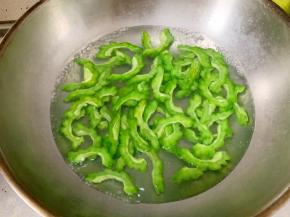 烧一锅水，放入一小勺食盐，水开后倒入苦瓜片，焯水30秒左右。然后捞出冲凉水降温备用。苦瓜焯水之后，苦味会大大减轻，适口性更强。但一定注意不要时间过长，焯水时间长了就把苦瓜煮熟了，吃起来就不脆了。焯水之后最好能浸泡在冰水中，更能保持脆爽的口感和翠绿的颜色。