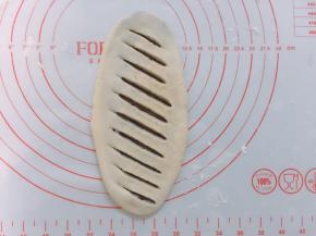 案板上撒上少许面粉，面团按扁后擀成牛舌状，边擀边排气，防止爆出豆沙，然后用刀划出条状切口，不要太重划，注意别把下层割开了