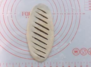 案板上撒上少许面粉，面团按扁后擀成牛舌状，边擀边排气，防止爆出豆沙，然后用刀划出条状切口，不要太重划，注意别把下层割开了