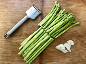 将洗干净的芦笋一分为二，根部用削皮刀去皮，大蒜切片。