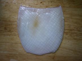 把鱿鱼上面尖尖的那个部位切下来，然后把鱿鱼整个摊开，在鱿鱼的肚子上划井字打花刀，记得不要切断了。有黑膜的那面是背部，没有黑膜那面就是肚子。