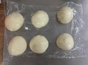 将面团拿出排气，分割成80G每个的小面团，滚圆后盖保鲜膜松弛15分钟。