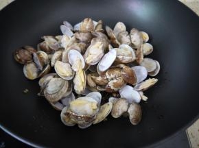 豆瓣酱炒出红油后把花甲放进锅里，大火翻炒，然后再加一点料酒翻炒均匀。