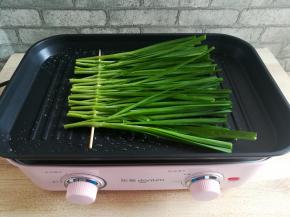 加热东菱多功能锅，烤盘里刷适量的油，放入一串韭菜，转大火用锅铲稍微压一下韭菜，让其均匀受热