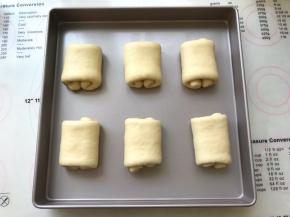 之后将卷好的面团卷曲面朝下摆放在方盘内，盖保鲜膜室温发酵至两倍大