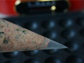 多用锅放上丸子烤盘，然后刷上一层薄油，预热好之后转中火，将拌好的肉馅装至裱花袋里，然后再剪一个大口。