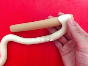 拿好火腿肠，接着把面团的一头按压薄，贴在火腿肠上，圈卷在火腿肠上面，收口压在下