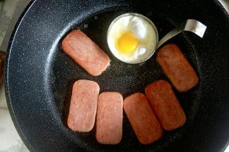 放入午餐肉片煎至两面金黄，煎蛋器中打入一个鸡蛋煎熟。
