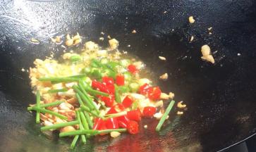 倒入青红小米辣、葱段和花生碎，炒香