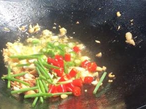 倒入青红小米辣、葱段和花生碎，炒香