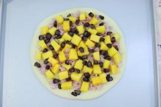 烤好的披萨皮，表面抹上披萨酱，摆上芝士碎，再铺上水果粒和黑玉米，培根。