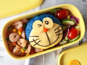 把多啦梦饭团放在便当盒中间，把配菜和蔬菜沙拉分别放在饭团的两边，把便当盒填满，这份萌萌的又有营养的便当就做好啦！
