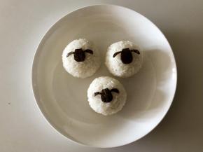 把海苔片对折，对称的剪出小羊肖恩的头，剪出三个，放到饭团上。