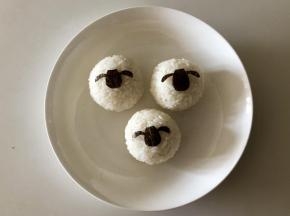 把海苔片对折，对称的剪出小羊肖恩的头，剪出三个，放到饭团上。