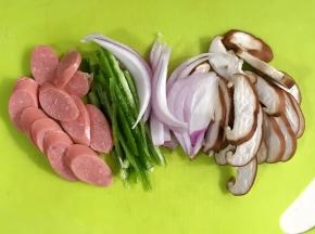 把蘑菇和青椒冲洗净沥干水分，用刀把蘑菇和香肠切片，青椒和洋葱切丝。