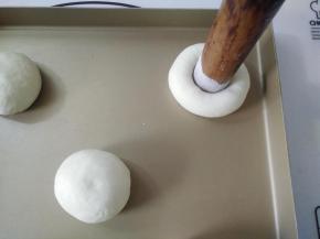 再将面团揉圆排掉里面的气体，把面团摆入烤盘，用擀面杖一头蘸面粉，用擀面杖在面团中间按压一个洞。