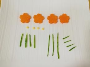 胡萝卜片用模具刻出花朵形状，从芝士片上用细吸管刻出四个小圆片做花心，用黄瓜皮剪出小花的枝干、叶子和小草。