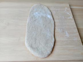 用手把面团里的气体挤压出来，把面团分成三份，放在室温下中间发酵15分钟。取1个面团在案板上擀成长椭圆形。