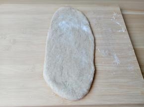 用手把面团里的气体挤压出来，把面团分成三份，放在室温下中间发酵15分钟。取1个面团在案板上擀成长椭圆形。