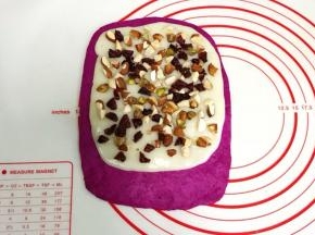 把擀开的麻薯片铺在面片上，放上切碎的杏仁、开心果和蔓越莓碎，然后轻轻按压下。